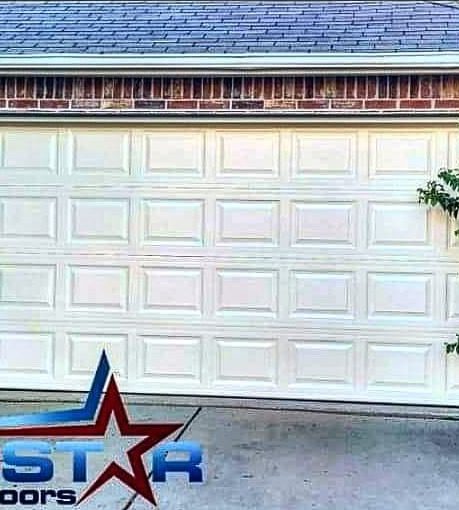 Repaired white raised-panel garage door on a brick home
