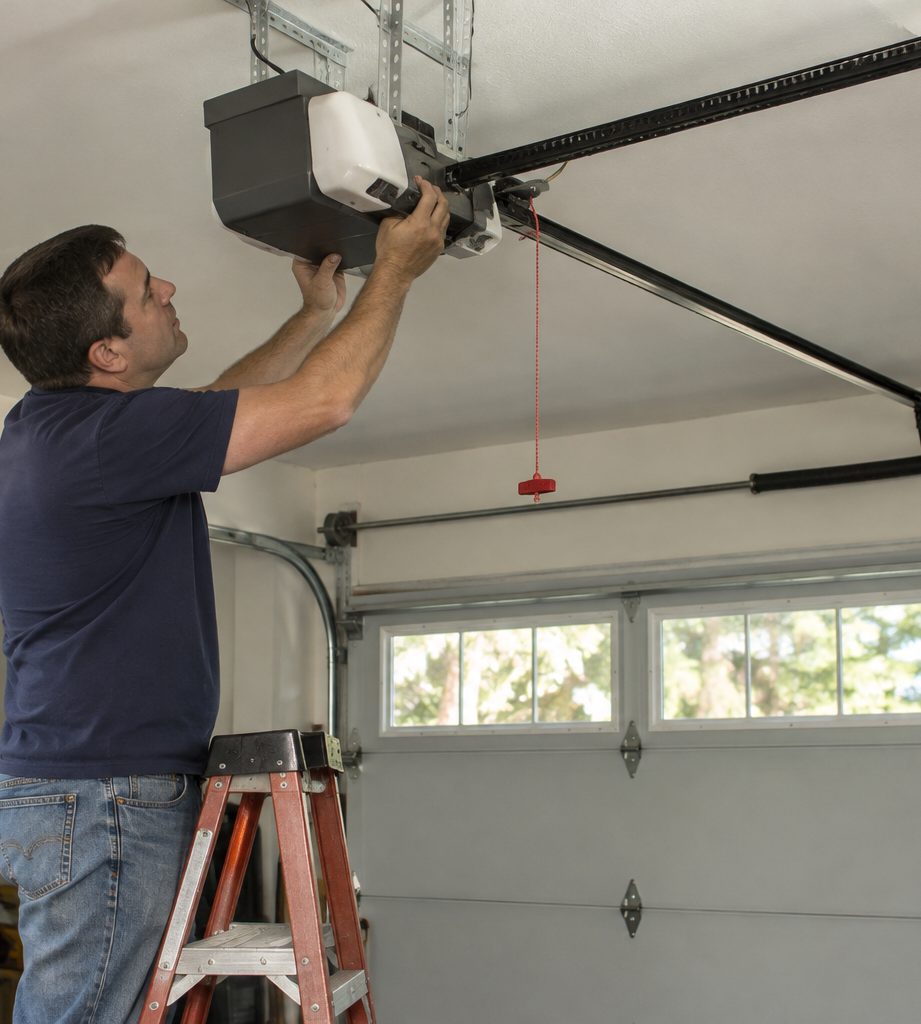 Technician adjusting a garage door opener motor on a garage ceiling